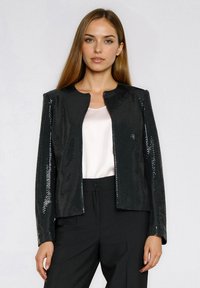 Czarna cekinowa kurtka z okrągłym dekoltem i długimi rękawami, zaprojektowana w dopasowanym fasonie z gładką podszewką. Stylizowana z jasnym topem.