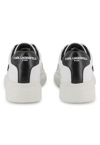 Λευκά και μαύρα αθλητικά παπούτσια με λείο δέρμα στο επάνω μέρος, στρογγυλεμένο σχήμα, μαλακό γιακά και λογότυπο στη φτέρνα. Επίπεδη λαστιχένια σόλα.