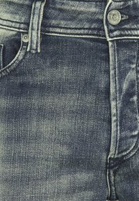 Mörkblå denimjeans med en klassisk femfickdesign, silverknappar och ett strukturerat tyg med blekningsaccenter.