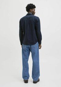 Donkerblauwe lange mouwen shirt en lichtblauwe losse spijkerbroek. Het shirt heeft een getailleerde pasvorm met knoopdetails; de spijkerbroek heeft opgestikte zakken en een relaxte snit.