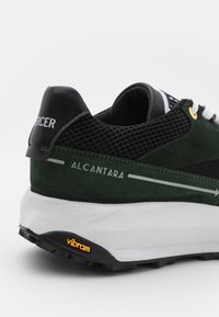 Zelené a černé tenisky z nubuku a síťoviny, s bílou mezipodešví a podešví Vibram. Viditelné kovové akcenty a značení.