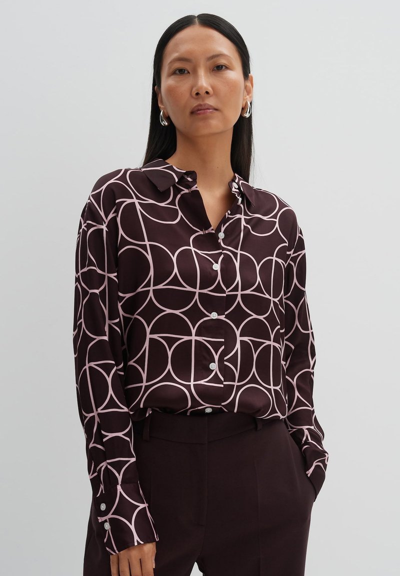 Dark brown button-up shirt with a pink geometric circle pattern, long sleeves, and a pointed collar. Smooth fabric with a glossy finish.