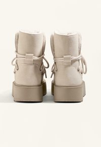 Beige Wildleder-Ankle-Boots mit einem flauschigen Futter, gepolstertem Kragen und Schnürdetails. Die Sohle ist dick und strukturiert, was Halt bietet.