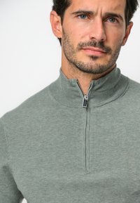 Grauer Zip-Hoodie mit Stehkragen, aus einem glatten, strukturierten Stoff, ausgestattet mit einem silbernen Metallreißverschluss und gerippten Bündchen.