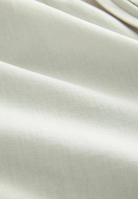 Světlý béžový materiál s hladkým, mírně texturovaným povrchem, který vykazuje jemný tkaný vzor a měkký pád.