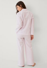 Lyserød pyjamas sæt med lodrette striber, lange ærmer og krave. Stoffet ser blødt og tekstureret ud. Bukserne er løstsiddende.