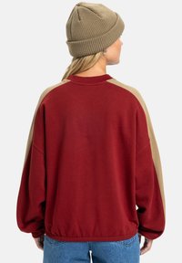 Bordeaux sweatshirt met beige schouderpanelen, oversized pasvorm, geribbelde halslijn, gestructureerde gebreide beanie, ontspannen mouwontwerp, casual stijl.