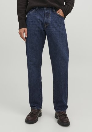 Vaqueros de mezclilla azul oscuro con corte recto, bolsillos frontales y cintura lisa. Combinados con zapatos marrones y un suéter oscuro texturizado.