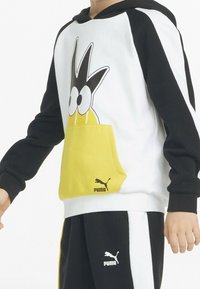 Bluza z kapturem z czarnymi rękawami, białym korpusem i dużą żó�łtą kieszenią z postacią z kreskówki. Czarny i biały logo na kieszeni.