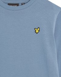 Sweatshirt bleu clair en tissu à la texture lisse. Il présente un petit logo brodé jaune sur la partie gauche de la poitrine.