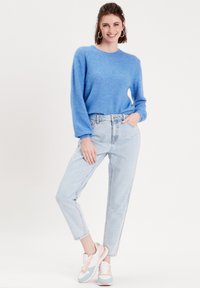 Pull en tricot bleu clair avec des manches longues, associé à un jean taille haute délavé et des baskets multicolores.