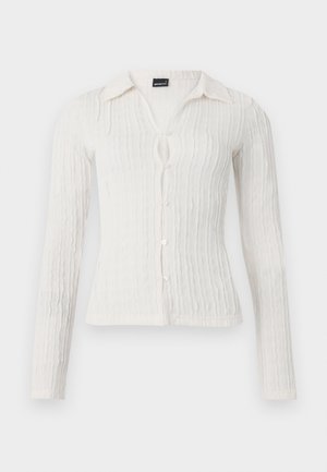 Long-sleeve white blouse with a textured ribbed design, collared neckline, button closure, and a small keyhole opening at the front.