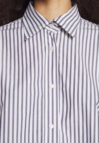 Primo piano di una camicia a righe verticali bianche e nere con colletto a punta e quattro bottoni bianchi visibili.