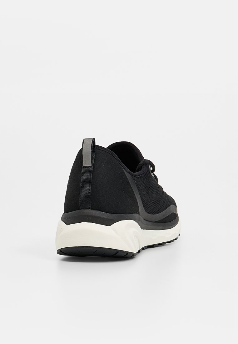 Zapatilla deportiva negra con parte superior de malla texturizada, suela blanca en contraste y una lengüeta en el talón para facilitar su uso.