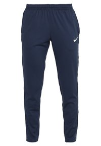 Marina atletiska byxor av slät tyg, med resårlinning och en vit Nike-logotyp på övre vänstra benet.