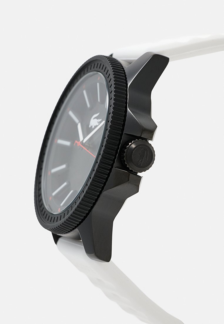 Montre analogique noire avec une lunette texturée, bracelet en silicone blanc, cadran noir avec index horaires blancs et accents rouges. Détail de couronne en relief inclus.