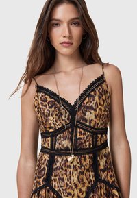 Vestido de padrão de leopardo com corpete ajustado e acabamento em renda, alças finas e saia rodada com detalhes em preto. Colar com pendente dourado adicionado.