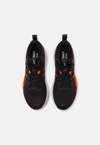 Zapatillas deportivas negras con acentos naranjas, parte superior de malla, cierre de cordones y una suela blanca ligera. Presenta tiradores en el talón.