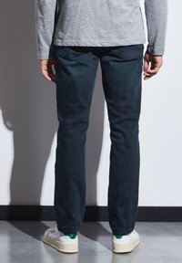 Tmavě modré džínové kalhoty s rovnýma nohavicema, zadními kapsami a jemnou texturovanou úpravou. Nosené s bílými teniskami.