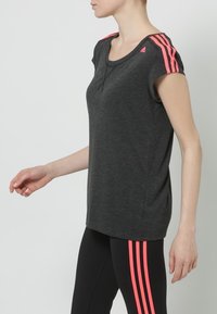 Camiseta atlética gris de manga corta con rayas rosas en los hombros. La tela parece suave, diseñada para la comodidad y la flexibilidad.