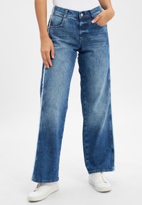 Jeans en denim bleu clair à jambe large avec une texture décolorée, dotés de deux poches latérales, d'une taille haute et de détails d'ourlet effiloché.