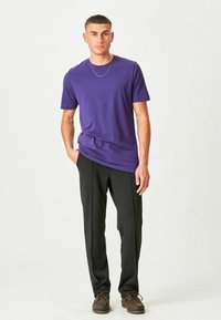 Fialové bavlněné tričko s krátkým rukávem, kombinované s černými kalhotami. K outfitu patří hnědé šněrovací boty. Jednoduchý design, hladká textura.