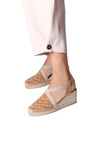 Beige espadrillos med kilklack, elastiska korsband, perforerat mönster på tån och en vävd jutesula.