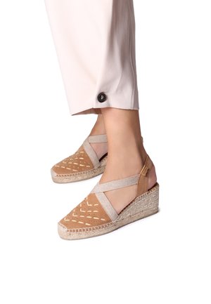 Beige espadrillos med kilklack, elastiska korsband, perforerat mönster på tån och en vävd jutesula.