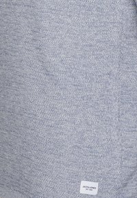 Tessuto a maglia grigio con un motivo testurizzato, dotato di un piccolo etichetta bianca in basso a destra che riporta "JACK & JONES EST. 1990."