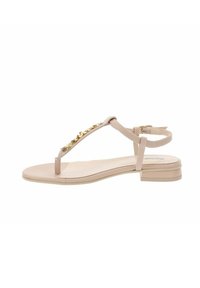 Sandalias planas de color beige claro con un diseño de tira en T, que presentan adornos en tono dorado, una correa ajustable en el tobillo y un tacón mínimo.