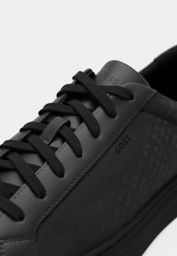 Sneaker in pelle nera con pannelli testurizzati, lacci neri piatti, punta rotonda e marchio in rilievo sui lati e sulla linguetta.