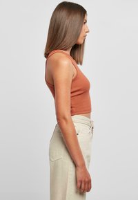 Brun ribbet crop topp kombinert med lysebeige høyhårede bukser. Sidesynsvinkel som fremhever toppens ermeløse design og glatte tekstur.