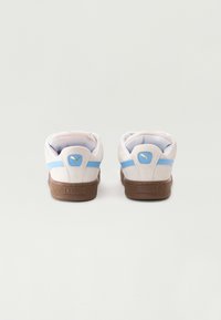 Hvite semsket sneakers med lyseblå striper, brune teksturerte gummisåler og gulllogo detalj på hælen. Bakvisning som viser glatt krage.