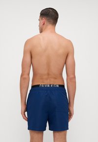 Calções de banho azul marinho com cintura elástica, apresentando o logotipo branco "CALVIN KLEIN", bolso lateral e textura de tecido suave.