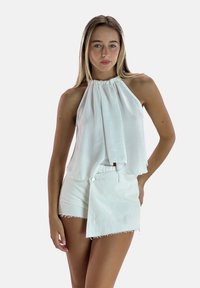 Witte mouwloze haltertop met gedrapeerde stof en een losse pasvorm, gecombineerd met witte shorts met een knoopdetail en een rafelige zoom.