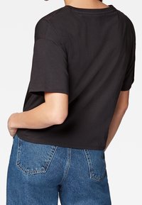 Černé zkrácené tričko z bavlny s krátkým rukávem a kulatým výstřihem. Nosené s modrými džíny, které mají zadní kapsy.