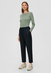 Groen lange mouwen top, donker geruiten taps toelopende broek met elastische taille, en beige sneakers. Eenvoudig ontwerp met zakken op de broek.