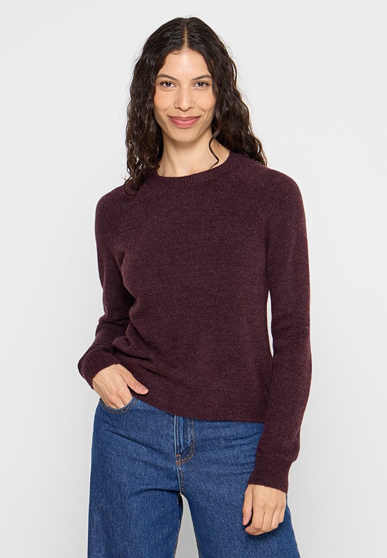 Bordeaux gebreide trui met een ronde halslijn en lange mouwen, voorzien van een geribbelde zoom en manchetten, gedragen over blauwe denim broek.