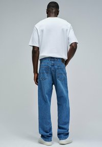 Camiseta de algodón blanca, corte relajado, combinada con jeans de mezclilla azul de corte holgado, con cinco bolsillos y costuras visibles en los bolsillos traseros.