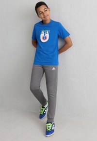 Plava pamučna majica s grafikom "Italija", sivi dukserica i plave atletske cipele s neonsko zelenim vezicama i bijelim prugama.