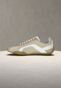 Baskets basses beige et blanches avec des lacets blancs et une semelle en gomme, vues de profil sur un fond neutre.