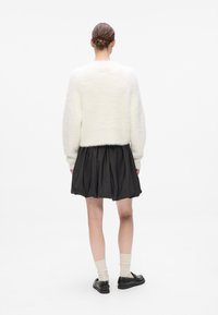 Hvit, fluffy genser, svart satengskjørt, kne-lang, samlet stoff. Sorte snøresko med kremfargede sokker. Enkel tekstur og design.