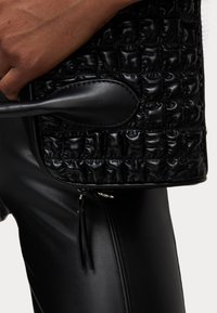 Bolso de mano de cuero trenzado negro con una superficie texturizada, asa delgada y cierre de cremallera. Cuenta con acentos de cuero liso en contraste.