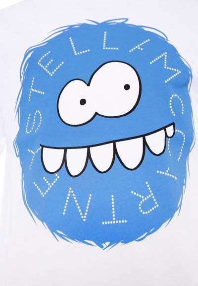 T-shirt bianco con un grande volto in stile cartoon blu, con occhi grandi e un ampio sorriso, circondato dal testo "STELLA McCARTNEY" con lettere a puntini.