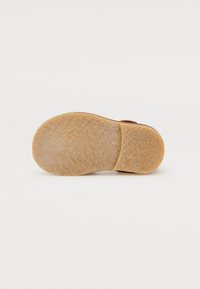 Semelle de chaussure en caoutchouc léger brun, avec une surface texturée. Forme arrondie avec un talon légèrement surélevé et des marquages du fabricant subtils.