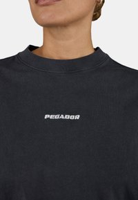 Sweatshirt en coton noir avec un col ras du cou. Présente un logo "PEGADOR" brodé en blanc sur la poitrine. Texture douce et unie.