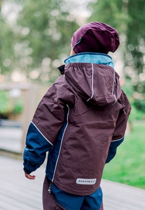 Brown waterproof jacket with navy accents and white piping, featuring a hood and elastic cuffs, worn by a child against a blurred outdoor background.