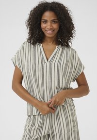 Blouse légère rayée en crème et gris foncé. Caractéristiques : décolleté en V, manches courtes et coupe décontractée. Le tissu texturé offre du confort.
