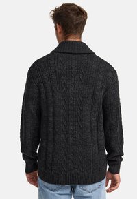Suéter negro de punto con un patrón texturizado, que presenta un cuello ancho, mangas largas y puños y dobladillo acanalados.