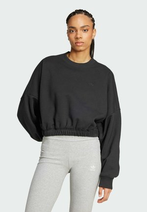 Sweatshirt noir court avec une coupe large et décontractée, ainsi qu'un ourlet côtelé. Associé à des leggings gris clair arborant un petit logo blanc.